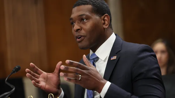 Man wearing a suit speaking into a microphone while seated