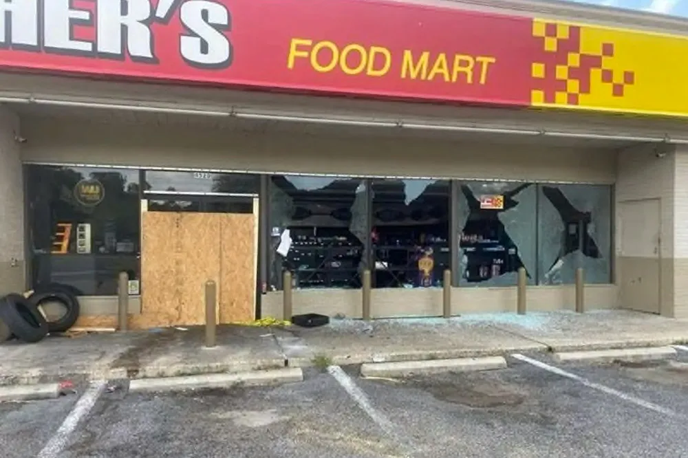 A convenience store&#x27;s front windows are broken, and a sign reads, &quot;food mart.&quot;