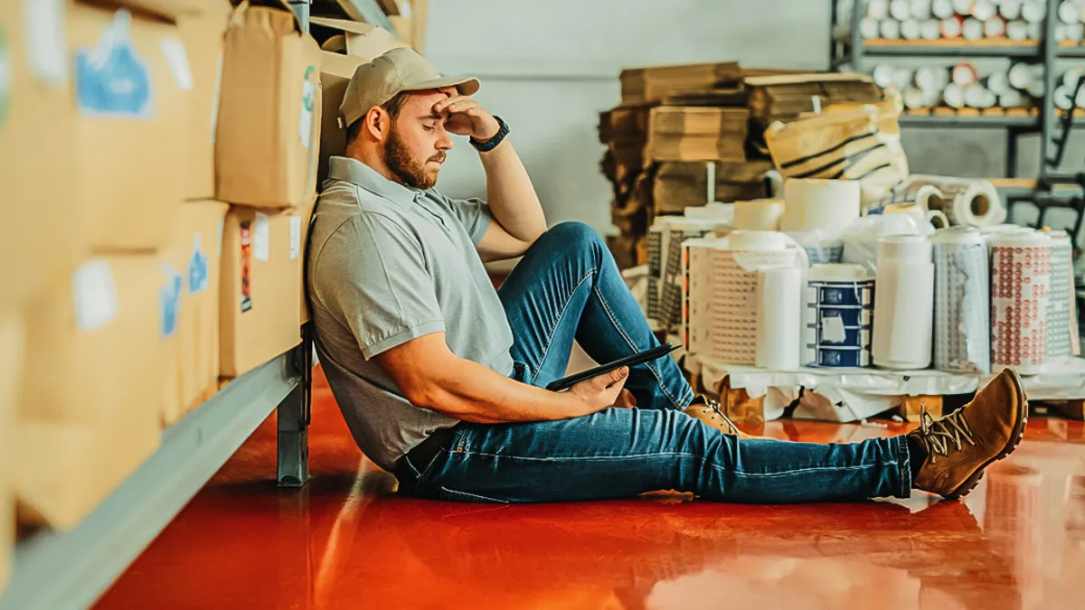 A worker lying on the ground with a tablet in hand with a look of burned out frustration.