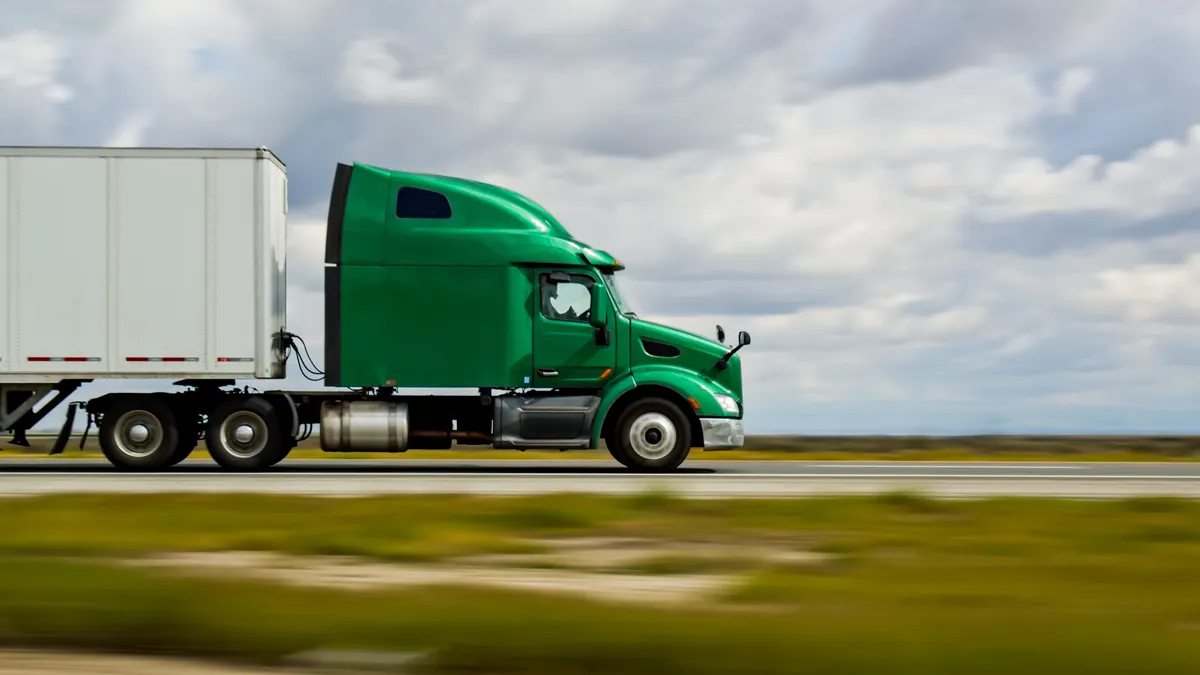 A green tractor pulling a trailer on a highway on an overcast day.