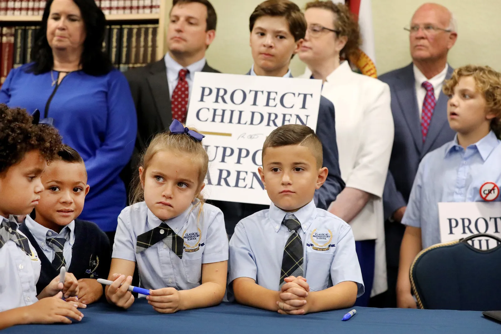 Children in uniforms congregate at a table with protest signs behind them