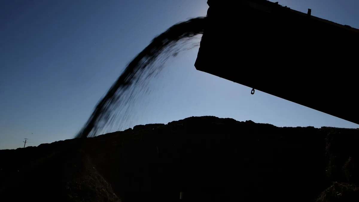 The silhouette of a process is visible where a dirt-like material flies off a conveyor belt into a large pile.