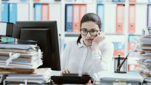 Young bored office worker sitting at desk and working, she is overloaded with paperwork