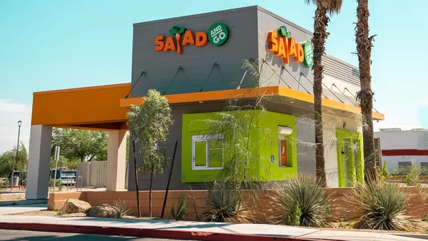 A daytime photograph of a small gray and orange building with "Salad and Go" signage.