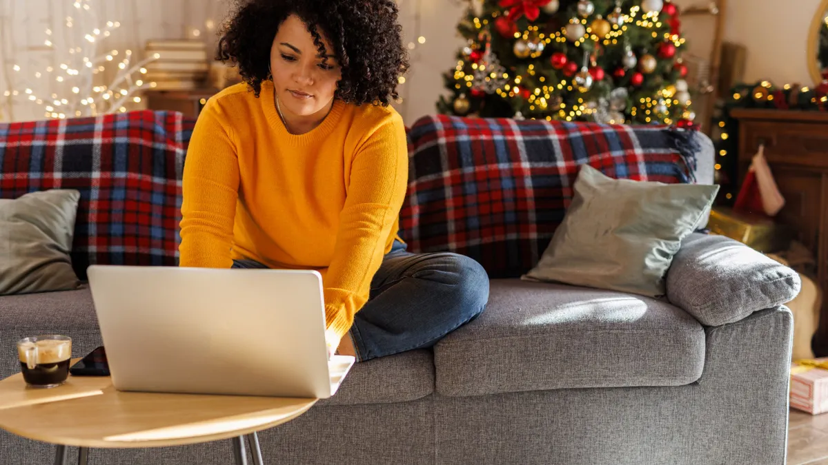 Woman sits on couch typing on laptop.