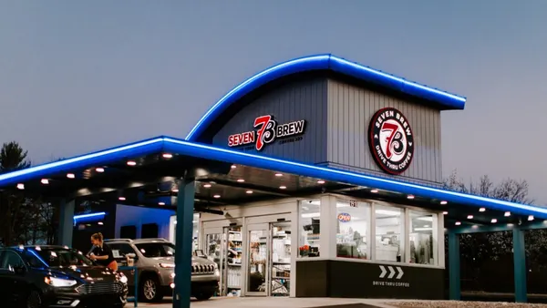 a drive-thru coffee shop with 7 Brew branding at dusk.
