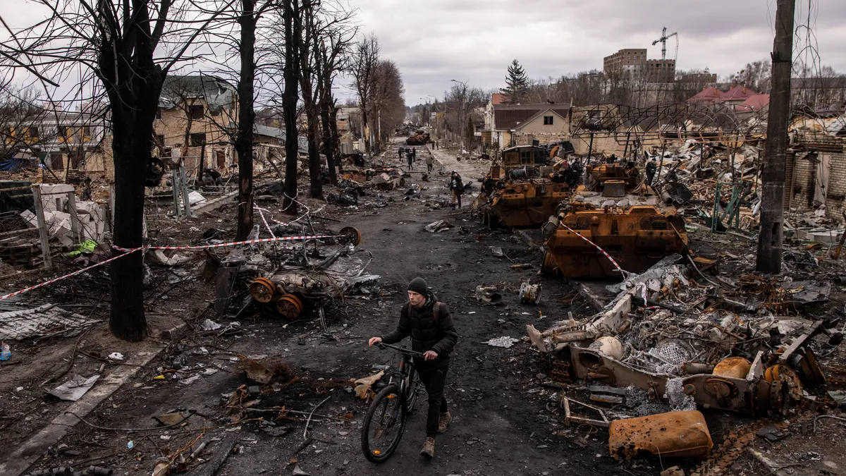 A man pushes his bike through debris and destroyed Russian military vehicles on a street on April 06, 2022 in Bucha, Ukraine.