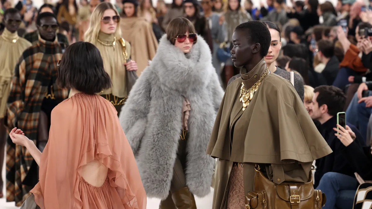 Models wear fur and sunglasses as they walk in circles on a brightly lit runway.