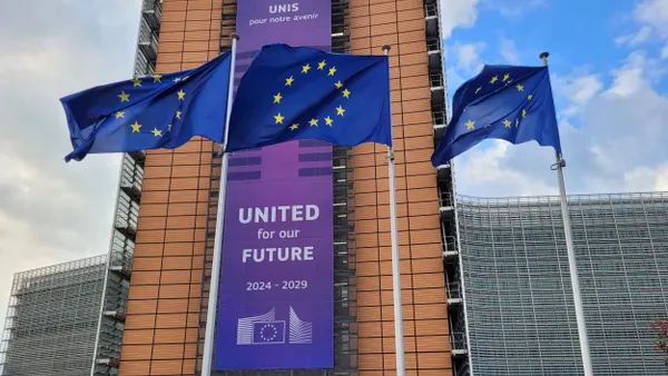 Three flags showing the European Union's logo in front of a building.