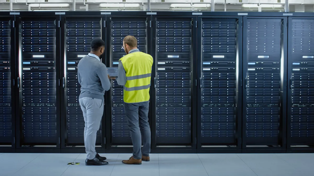 A data center technician and IT employee working next to data center server racks.