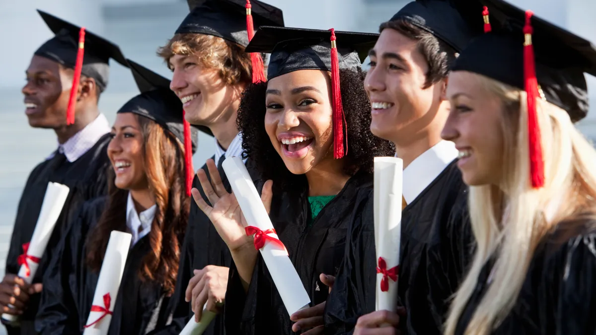 Multi-ethnic friends graduating together, in cap and gown. Main focus on African American girl in middle, waving at camera.