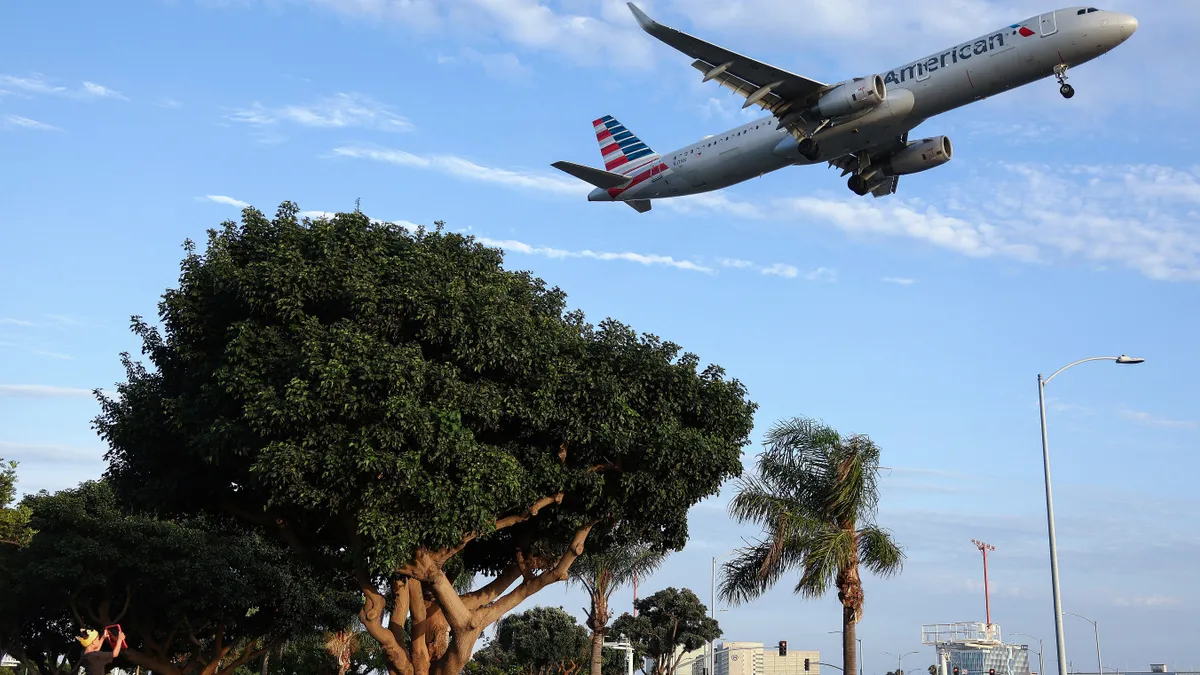 A child watches an American Airlines plane take off with trees visible outside of Los Angeles International Airport