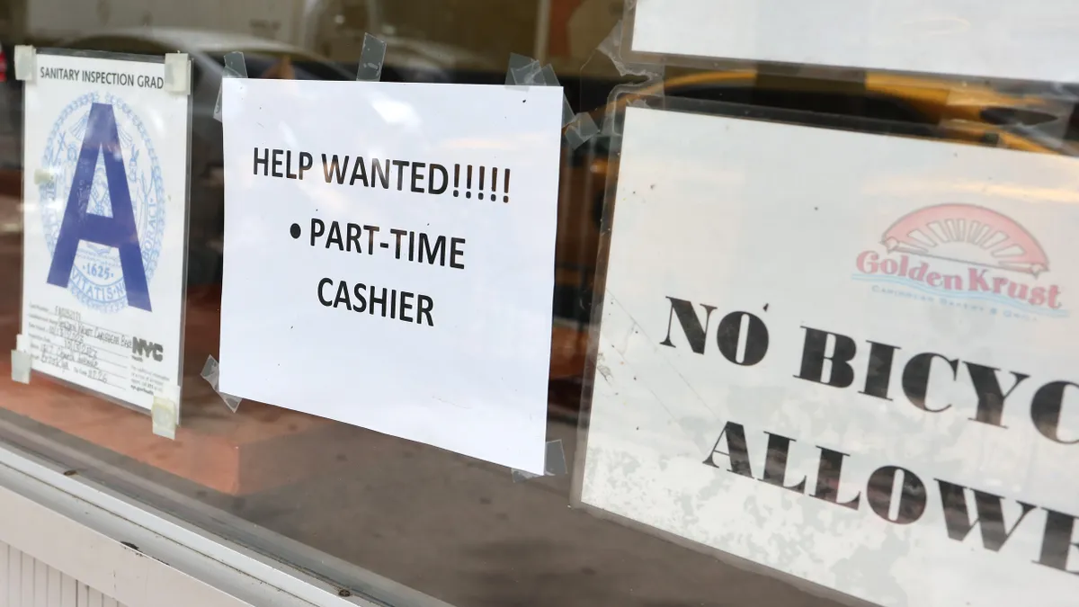 A help wanted sign hangs in a shop window.