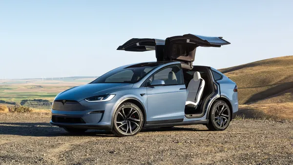 A blue Tesla Model X parked outdoors with its rear gull-wing doors fully opened.