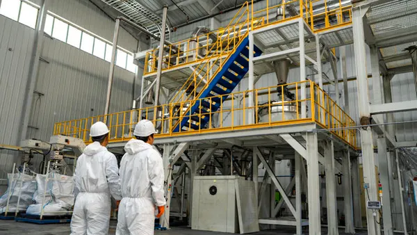 Workers in hard hats look up at equipment inside an industrial facility.