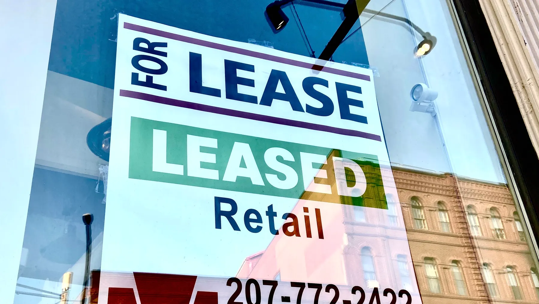 A "for lease" sign for on a retail store window, with a reflection of a building across the street.