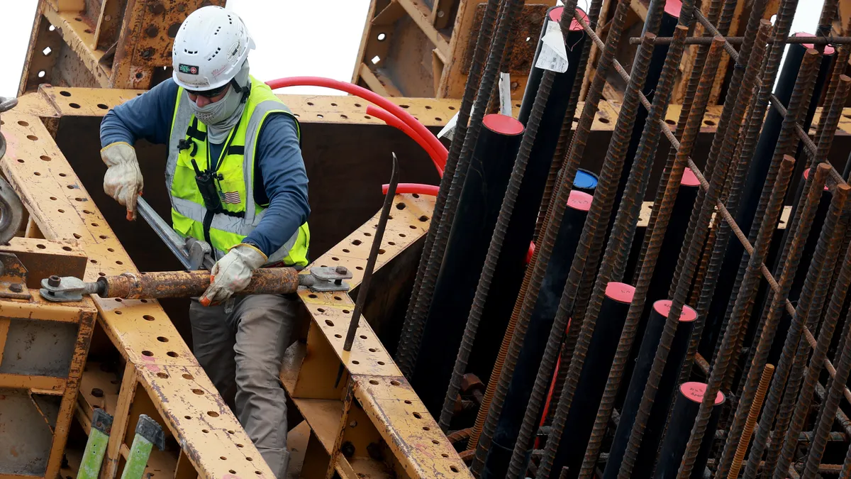 A construction worker in safety gear works in a tight spot on a bridge.