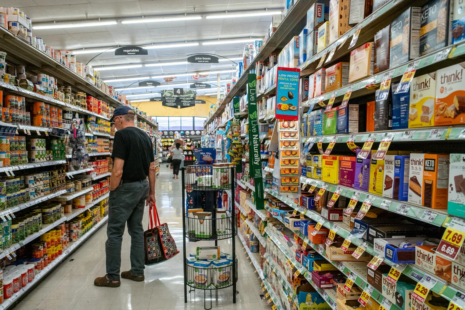 A person carrying a tote bag looks at items on a grocery store shelf