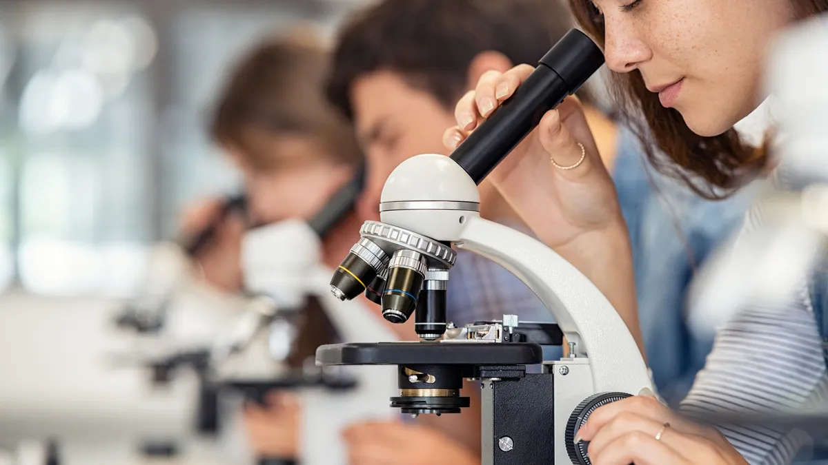 A high school student looks into a microscope in a classroom.