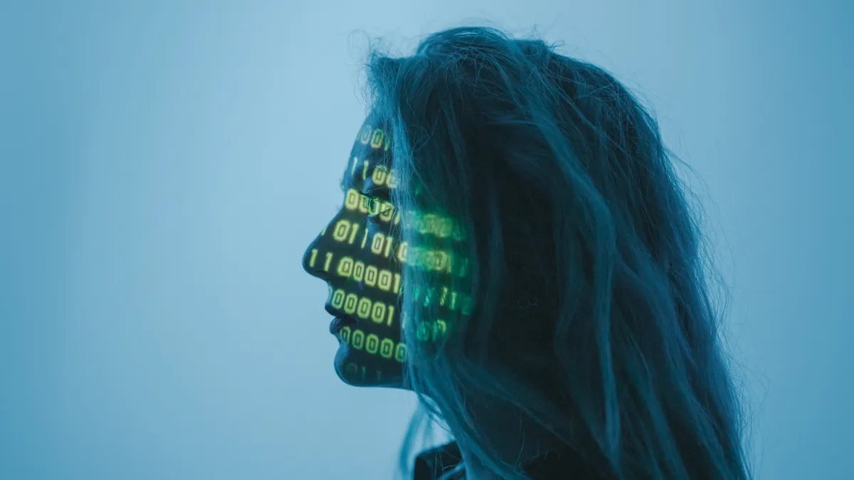 A person with long hair is in profile, with binary code projected on their face