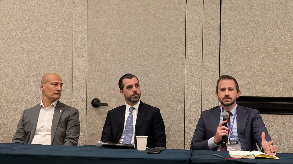 Three men sit behind a table in a conference ballroom