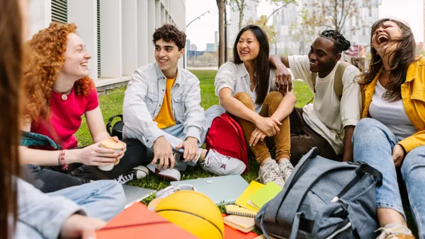 A diverse group of college students sitting on the grass outside a modern campus building.