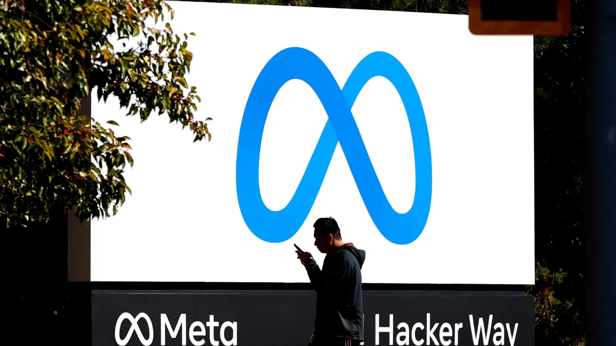 A pedestrian walks in front of a new logo and the name 'Meta' on the sign in front of Facebook headquarters