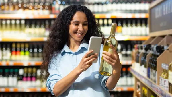Person looking at phone and holding wine bottle in grocery store