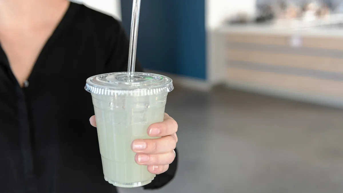 A person holds a clear beverage cup with a clear straw.