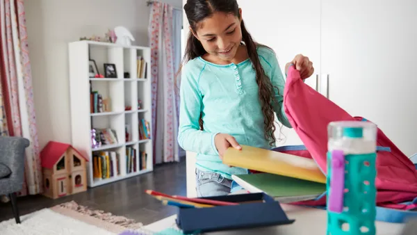 Young Girl In Bedroom Packing Bag Ready For School