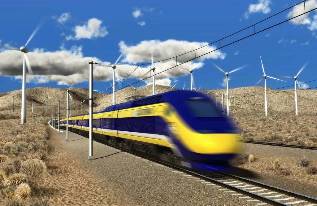 A sleek yellow and bluish purple train whizzes through the desert between tall white wind turbines in this rendering.