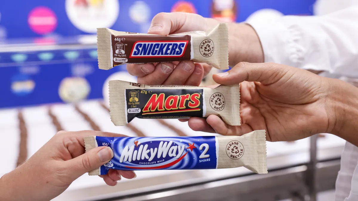 Hands hold a Snickers candy bar, Mars bar and Milky Way bar in paper-based packaging