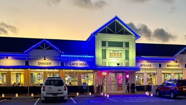 Exterior view of Mystic Diner Restaurant lit up with bright blue lights at sunset.