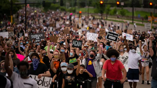 A large crowd of masked protestors holding signs related to the murder of George Floyd march in the street.