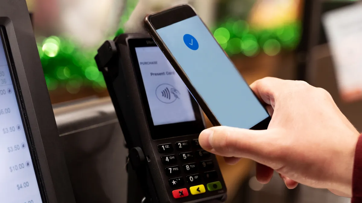 Person paying their phone at a self-checkout station in a supermarket.