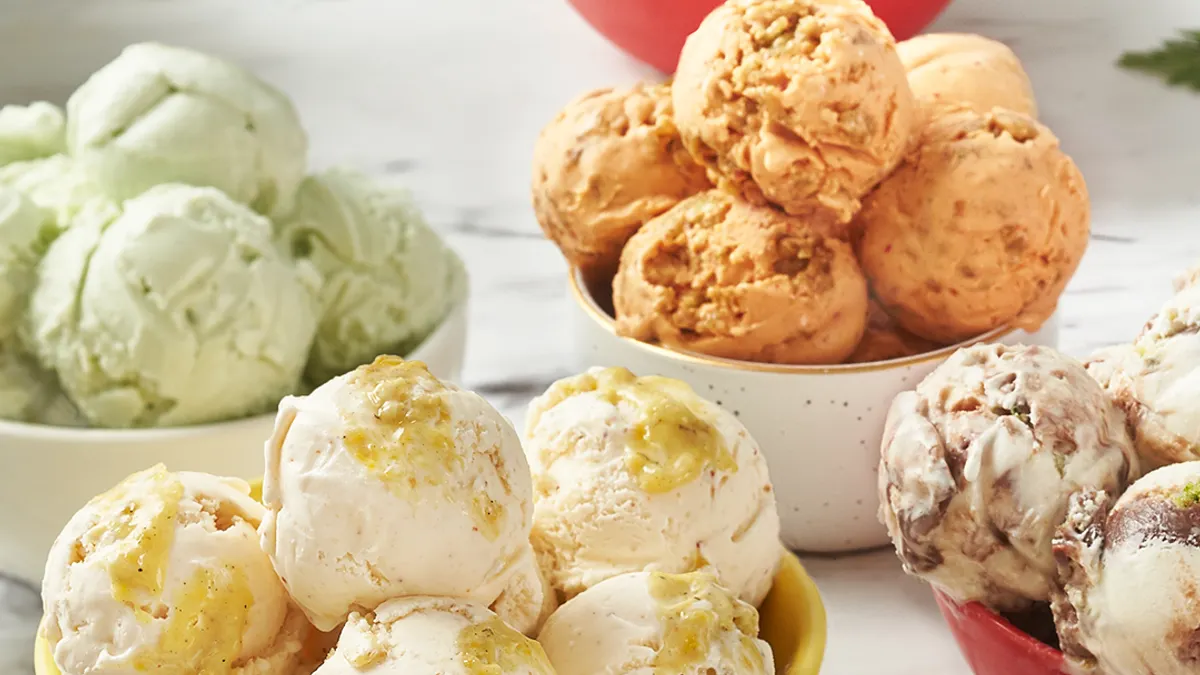 Bowls with scoops of a variety of ice cream flavors in different colors sit on a white marble countertop.