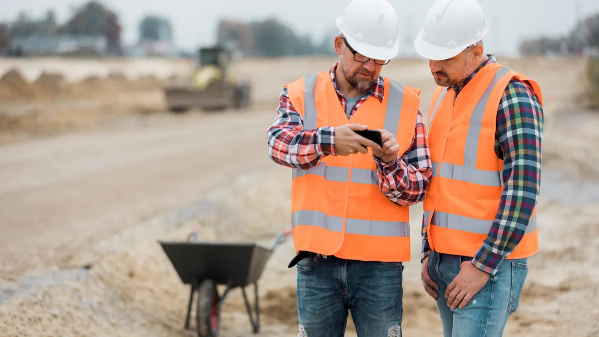 Two construction workers look at a phone