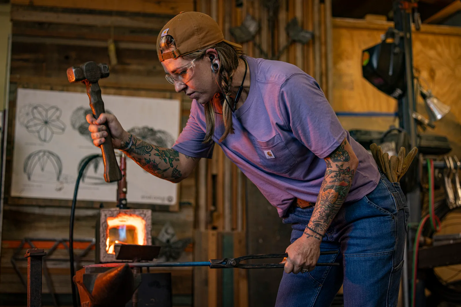 A person holds a hammer over a hot piece of metal.