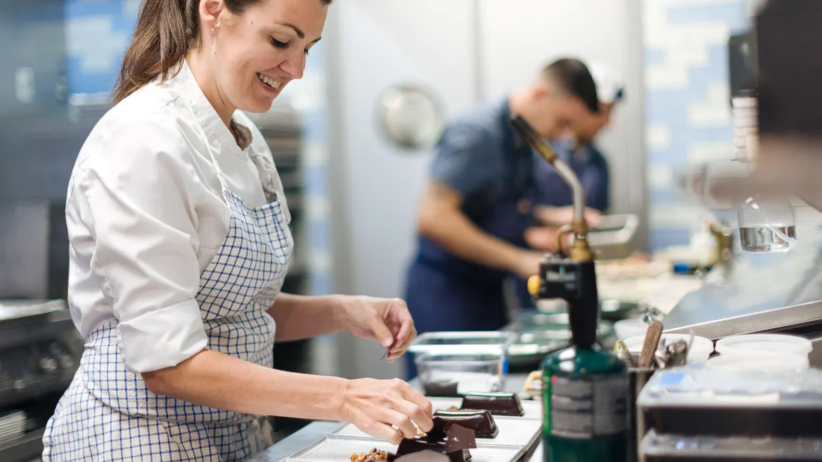A person stands over dishes of chocolate dessert inside a restaurant kitchen.