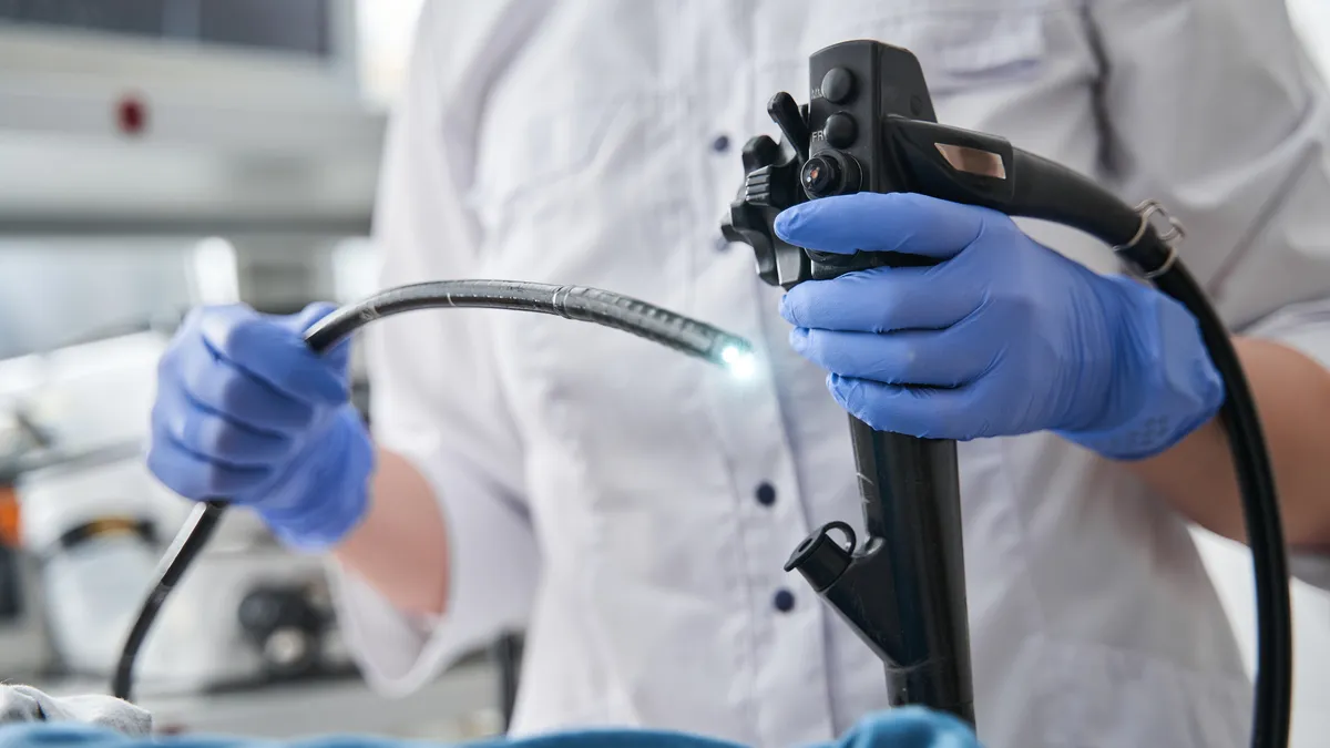 A person wearing blue gloves holds a long tube with a light at the end.