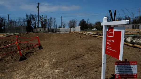 A red "For Sale" sign on a white post and a smaller sign about private fire debris removal in front of a bulldozed lot with burned trees in the background.