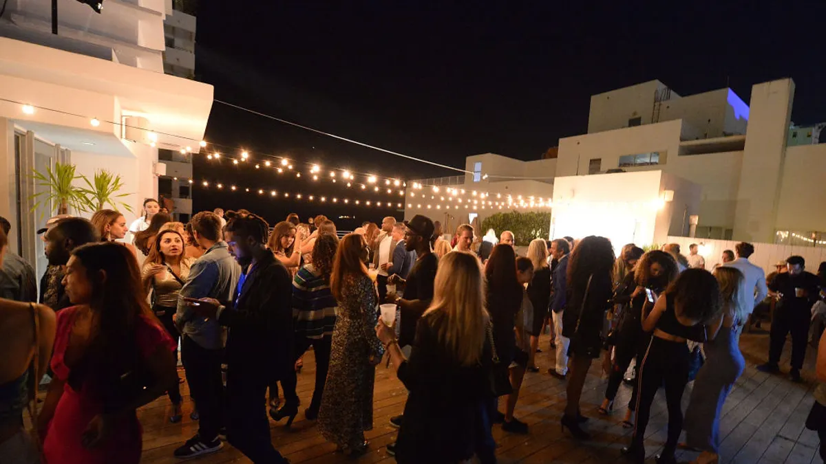 A crowd of people on a rooftop lit by string lights.
