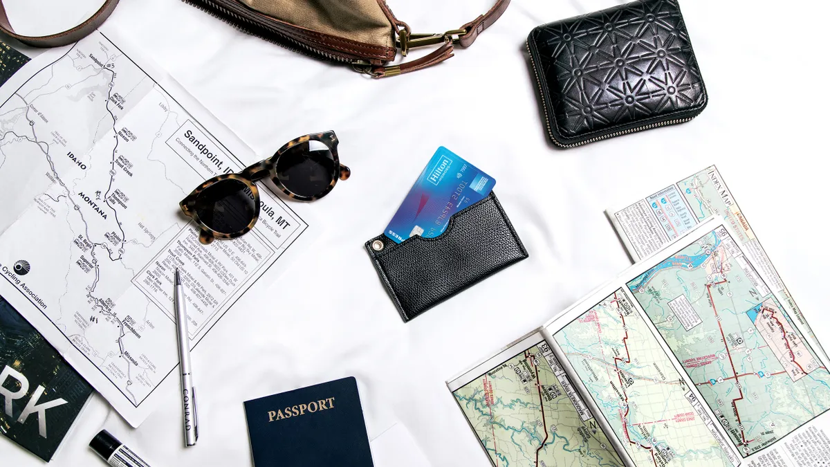 Photo of a Hilton Honors American Express card surrounded by travel items such as a passport, map, purse, sunglasses and bag