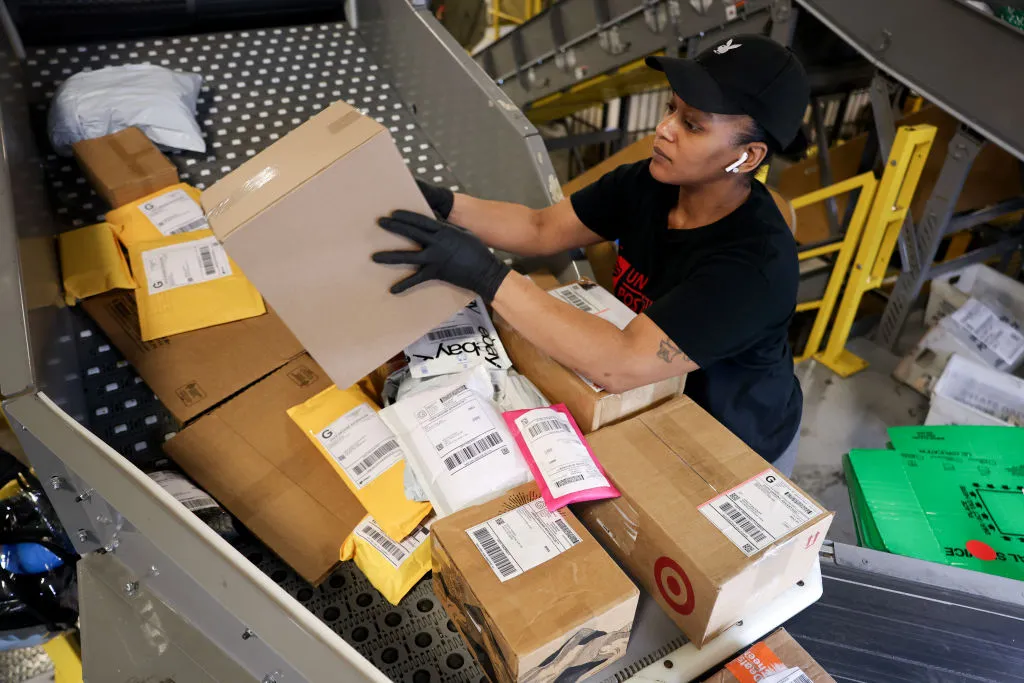 A person picks up and inspects a package from a pile on a conveyor belt.