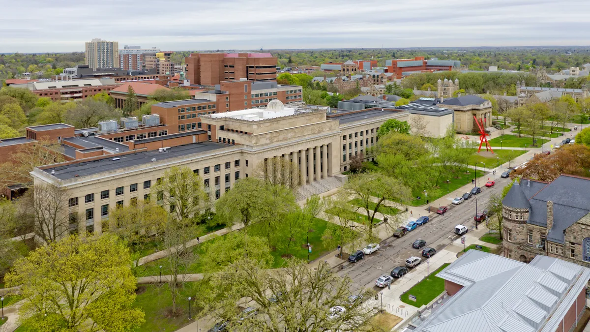 A bird's eye view of a large Brutalism academic building with cars lining the neighboring street