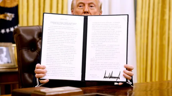 President Donald Trump's top portion of his face can be seen behind an open folder he is holding. His is in the Oval Office and seated as a desk.