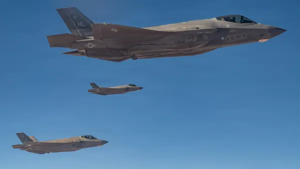 Three charcoal-gray fighter jets flying in a clear blue sky.
