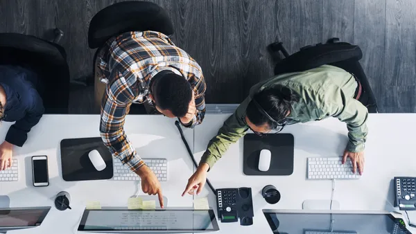 an overhead shot of two IT workers pointing at a monitor in an office setting