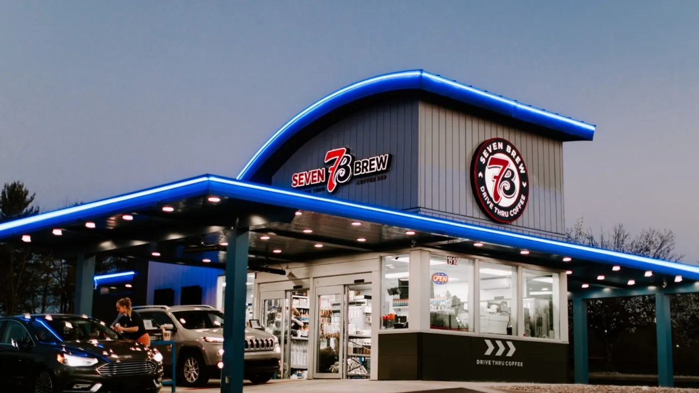 a drive-thru coffee shop with 7 Brew branding at dusk.