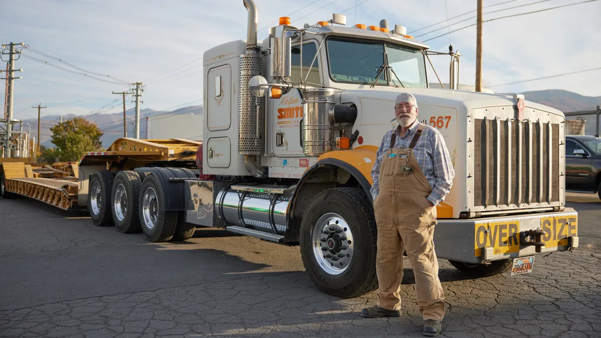 A person stands for a portrait in front of a large semi-truck.